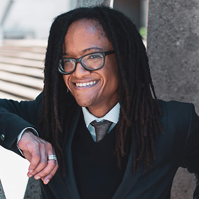 Picture of the artist Deon Best wearing glasses and looking over a lake